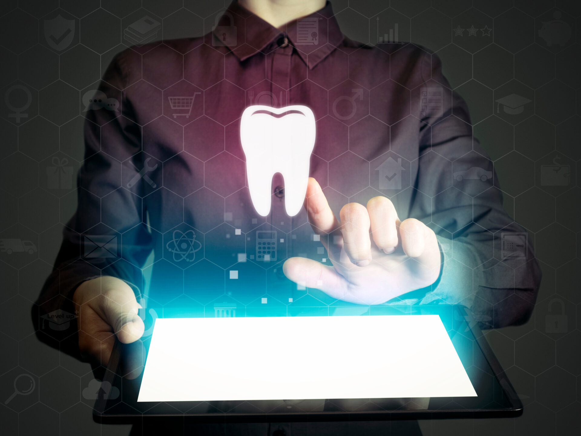 A person in a dark shirt uses a digital tablet, with a glowing tooth icon and virtual interface graphics hovering above the screen, symbolizing digital dental technology.