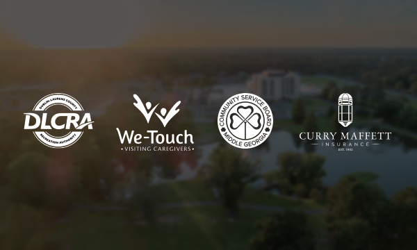 Four business logos—DLCRA, We-Touch Visiting Caregivers, Community Service Board Middle Georgia, and Curry Maffett Insurance—appear in white on a blurred park background with water and trees.