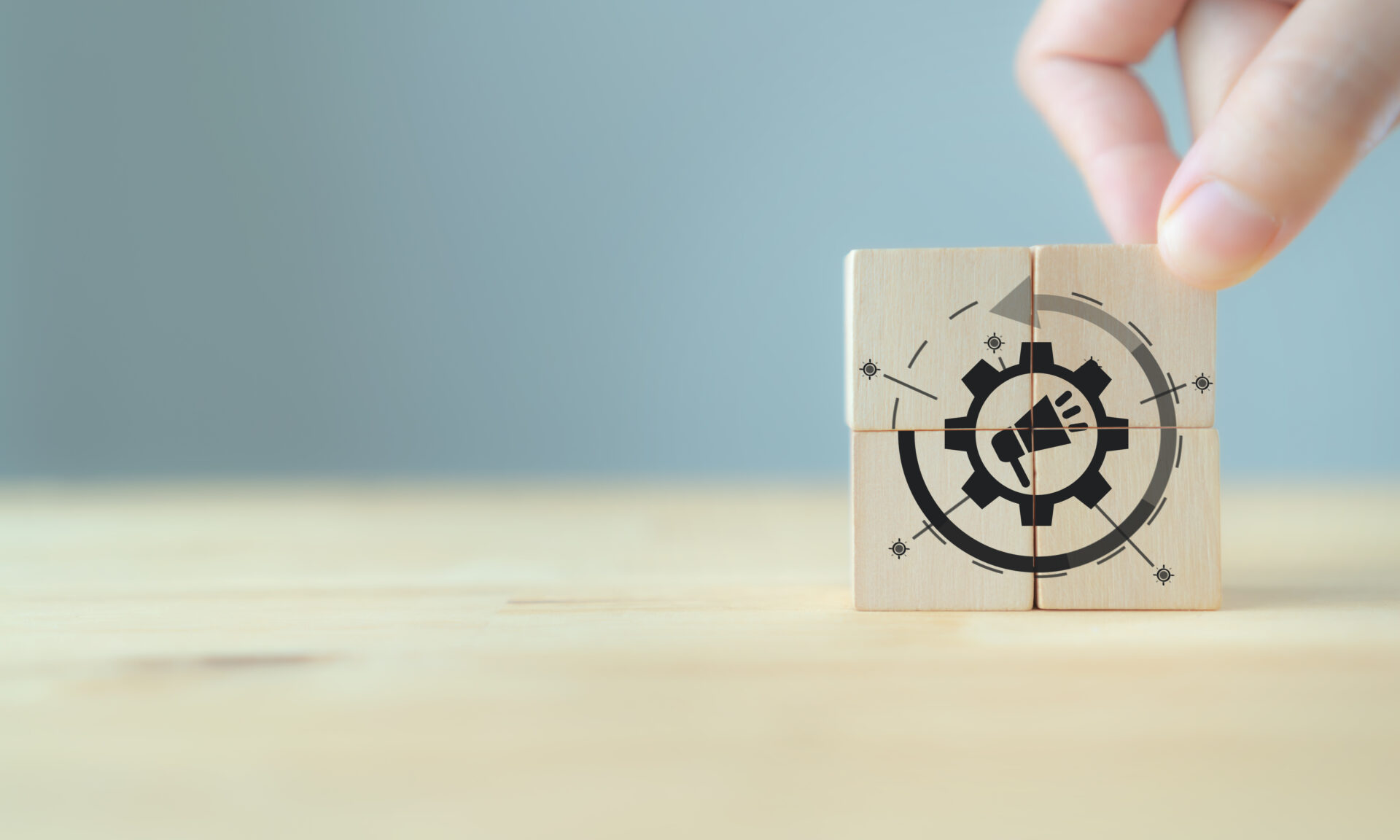A hand arranges four wooden blocks on a light surface, forming a gear with a megaphone symbol, suggesting marketing automation and tracking