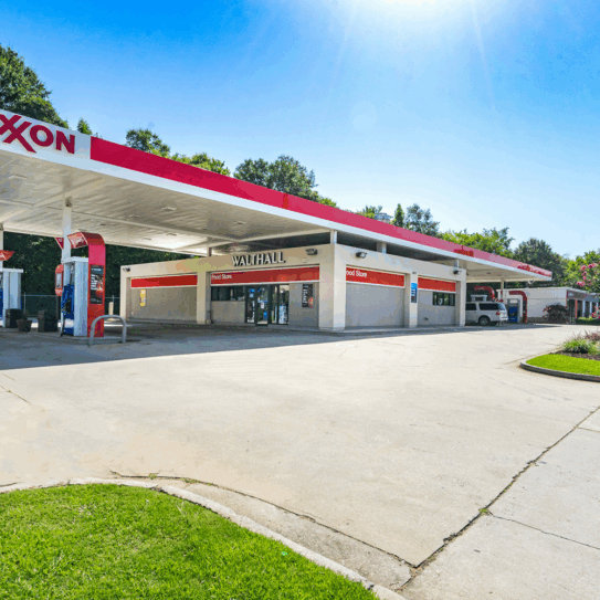 A sunny day at Walthall convenience store and Exxon gas station in Macon, GA. Clean pavement, service bays, American flag, and trees in the background.