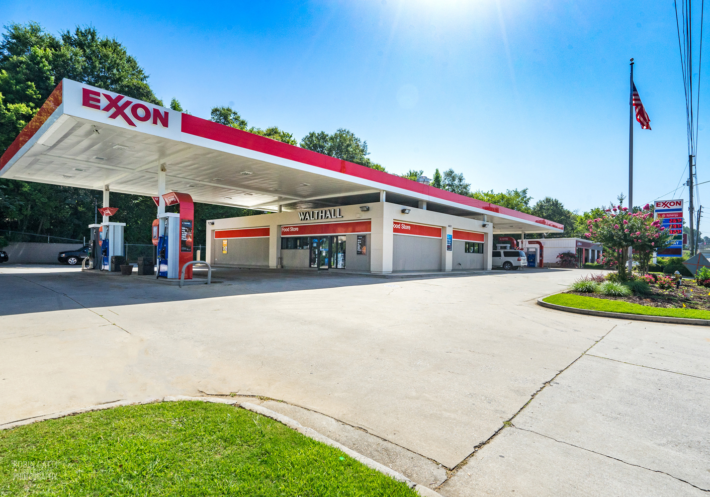 A sunny day at Walthall convenience store and Exxon gas station in Macon, GA. Clean pavement, service bays, American flag, and trees in the background.