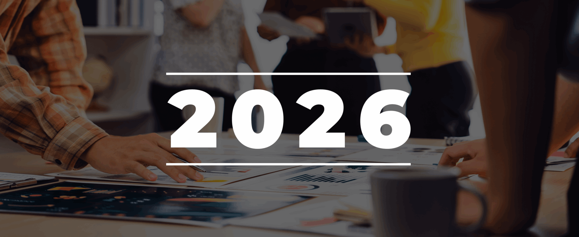 Large white text reading 2026 is overlaid on people working at a table with documents, graphs, and coffee, implying 2026 planning.