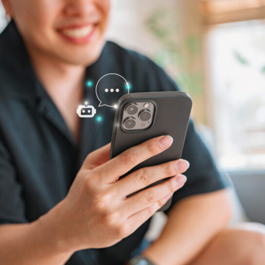 A smiling person holds a smartphone with chat and camera icons floating above it, suggesting social media. Softly blurred background.
