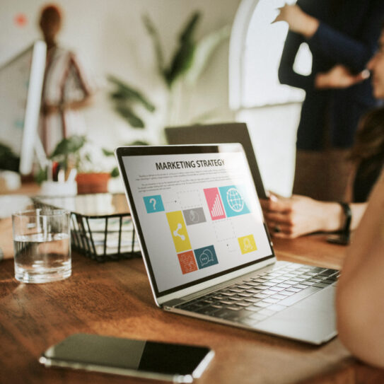 Closeup of a person's laptop in a meeting with a marketing partner. The screen has several icons on it with the heading Marketing Strategy