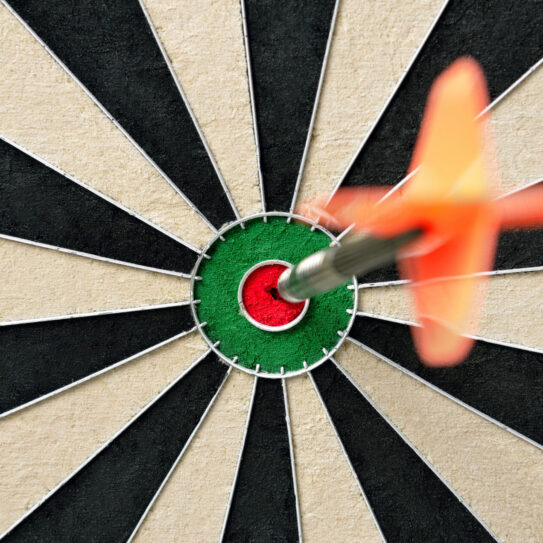 A red dart with orange flights sticks in the bullseye of a black and white dartboard, shot from above to emphasize precision. Visually signifying brand clarity.