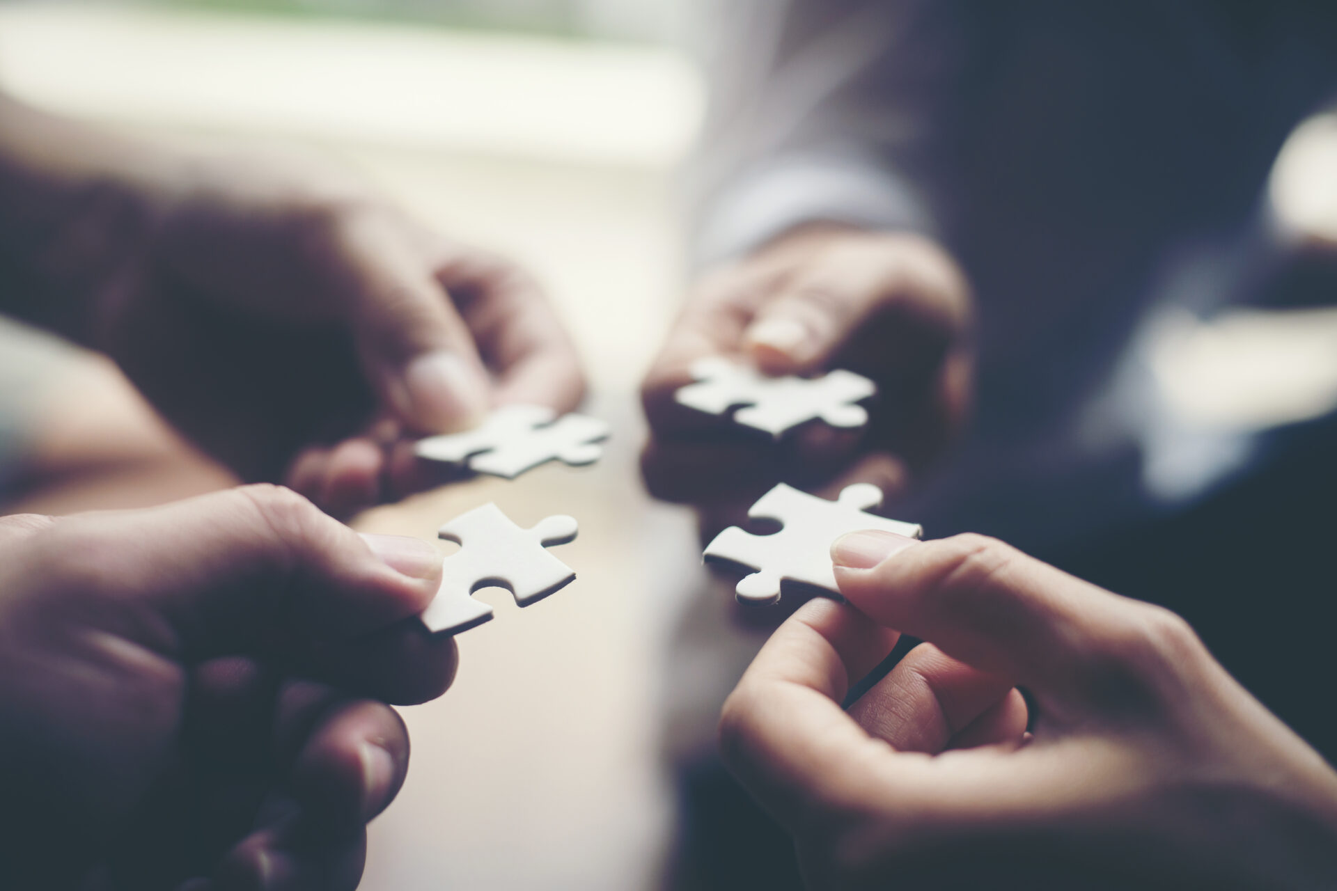 Close-up of four hands holding puzzle pieces, positioned to connect them, representing teamwork, collaboration, and the 4 pillars of a marketing partnership.