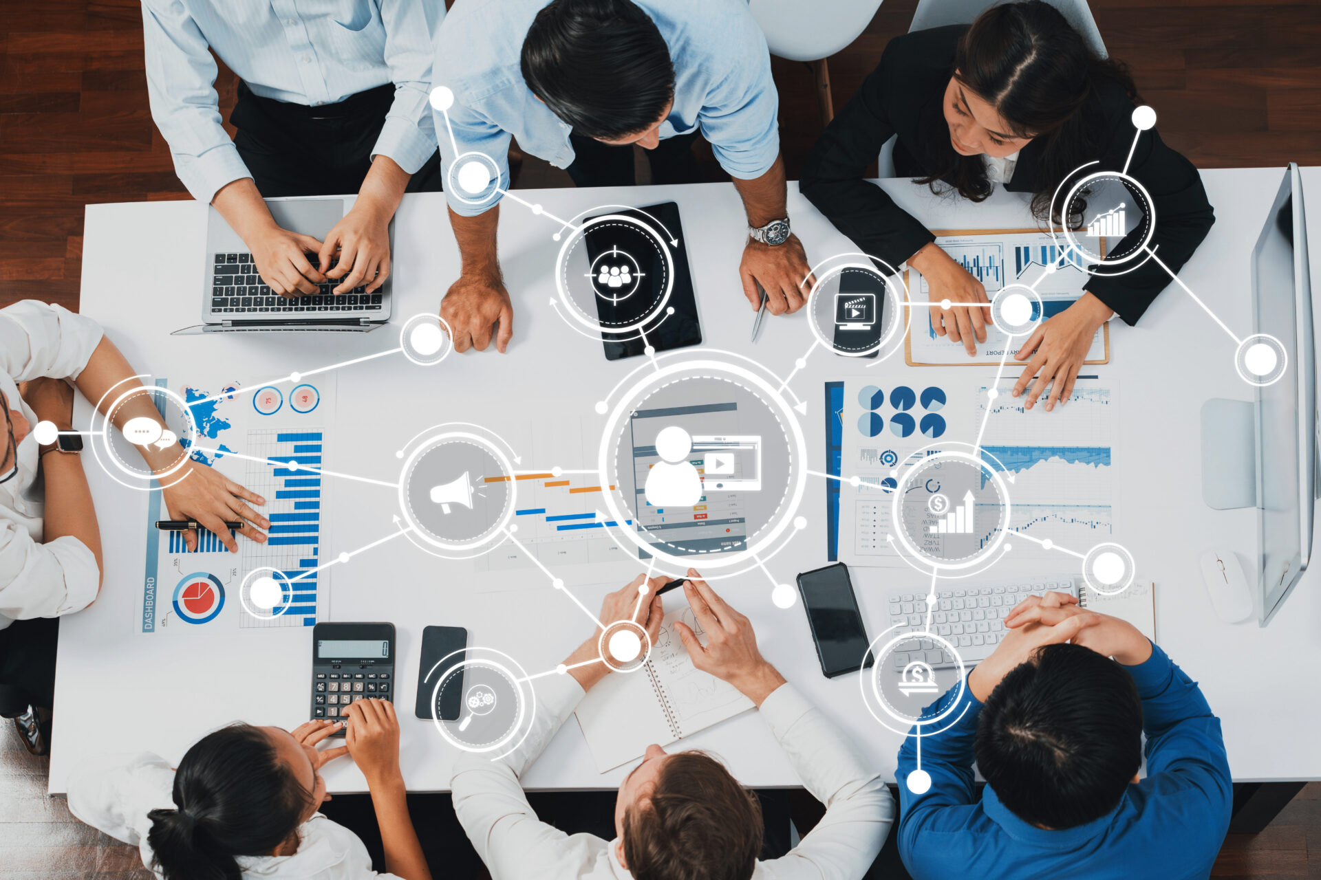 Group collaborating at a table with laptops, documents, and graphs, overlaid with digital network icons showing data sharing.